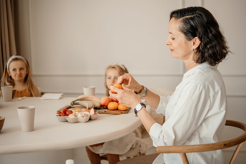 Family assistant maakt fruit klaar voor twee meisjes aan de eettafel