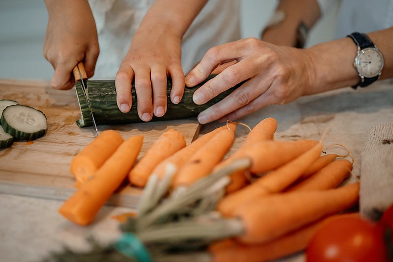 Handen snijden courgette en wortels op een houten plank