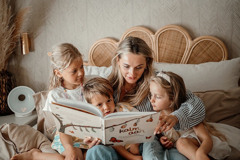Vrouw leest op bed een prentenboek voor aan drie kinderen